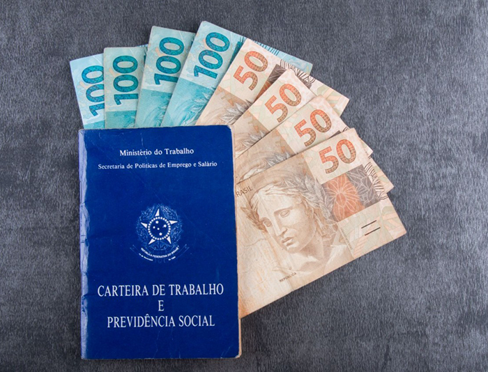 Carteira de Trabalho e Previdência Social ao lado de cédulas de dinheiro brasileiro